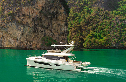 An Aquila 44 power catamaran cruising through clear bluish-green water from right to left with rocky cliffs in the background