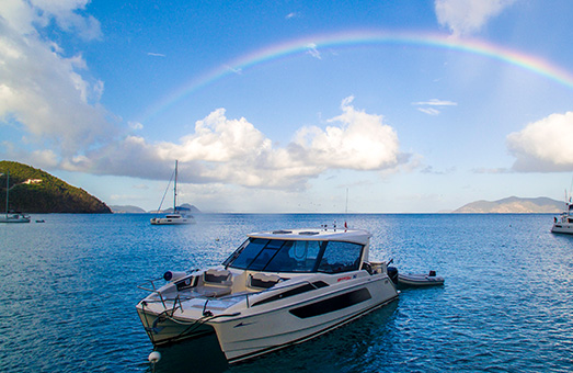 An Aquila 36 power catamaran in the blue water of the British Virgin Islands, with a rainbow overhead