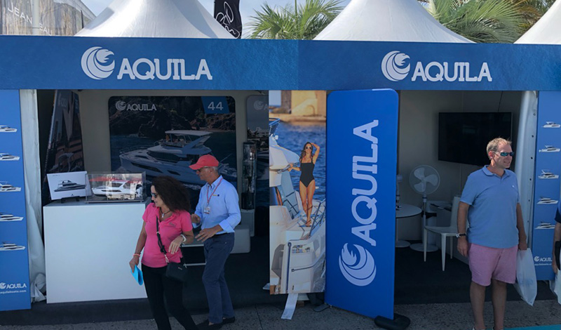 the aquila booth at the cannes yachting festival with people walking in and out of the blue tent