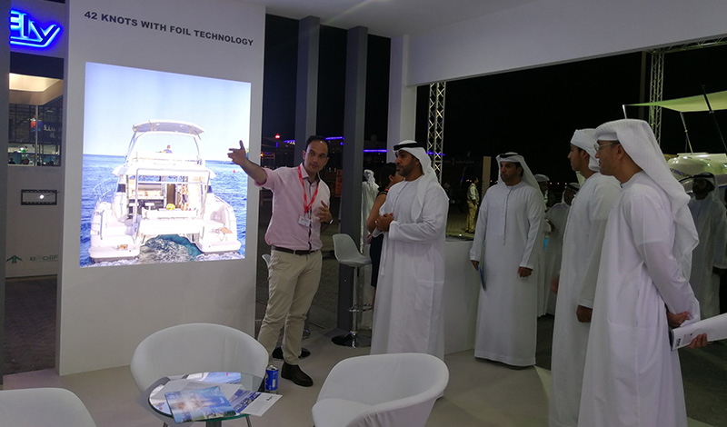 a group of men in the aquila booth at a boat show with a photo of an aquila power catamaran on the wall next to them