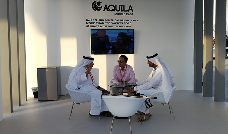 three men seated around a table at a boat show in front of a sign saying aquila