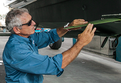 A man in a blue shirt holding a piece of metal up to the hull of a boat in a warehouse