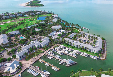 Aerial view of Captiva Island, with docked boats at the marina, a golf course in the background, and beautiful blue water around it