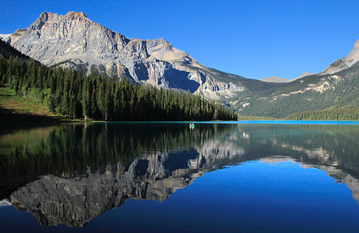A landscape in the Pacific Northwest, with evergreen trees, rocky mountains, and clear blue water